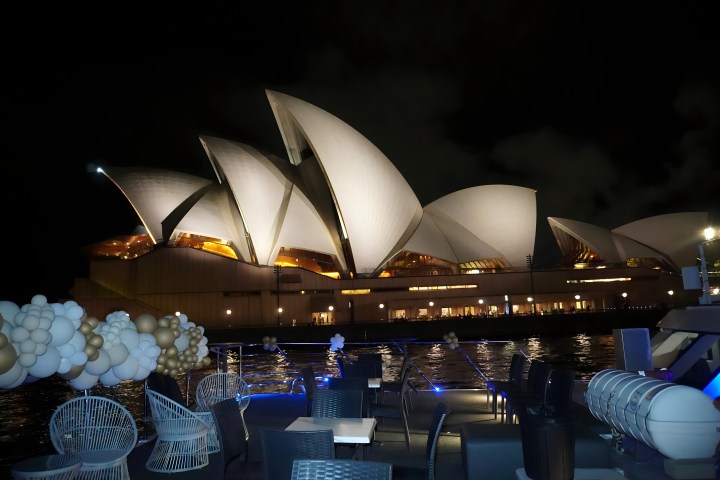 Sydney Opera House at night, seen from a boat with white and gold balloons.