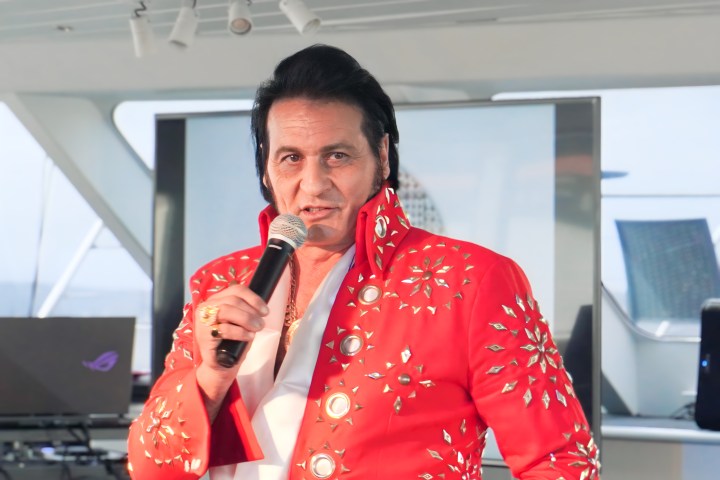 Man in red studded outfit holding a microphone, performing indoors.