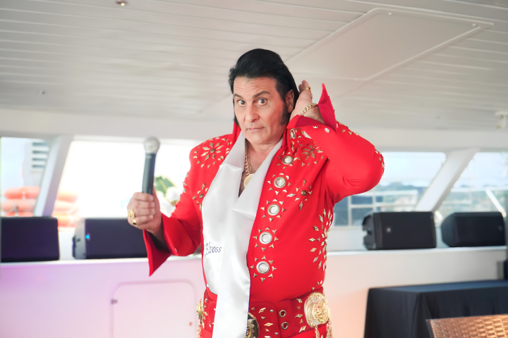 Man in red bedazzled suit holding a microphone on a boat.
