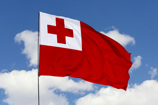 Flag of Tonga waving against a blue sky with white clouds.
