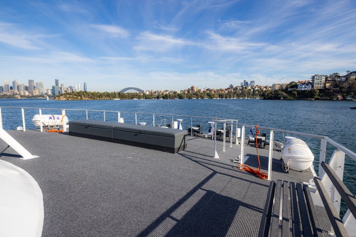 Boat deck with city skyline and harbor bridge in the background on a sunny day.
