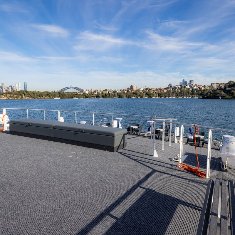 Boat deck with city skyline and harbor bridge in the background on a sunny day.