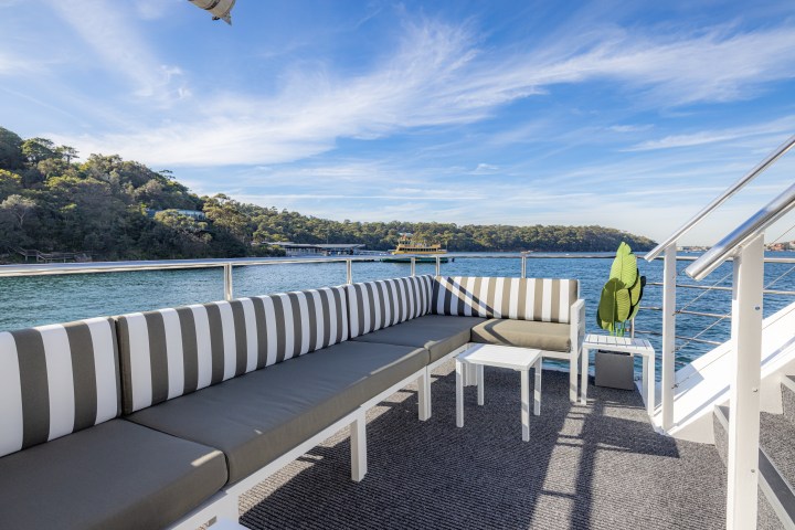 Outdoor seating on a boat with striped cushions, overlooking water and hills.