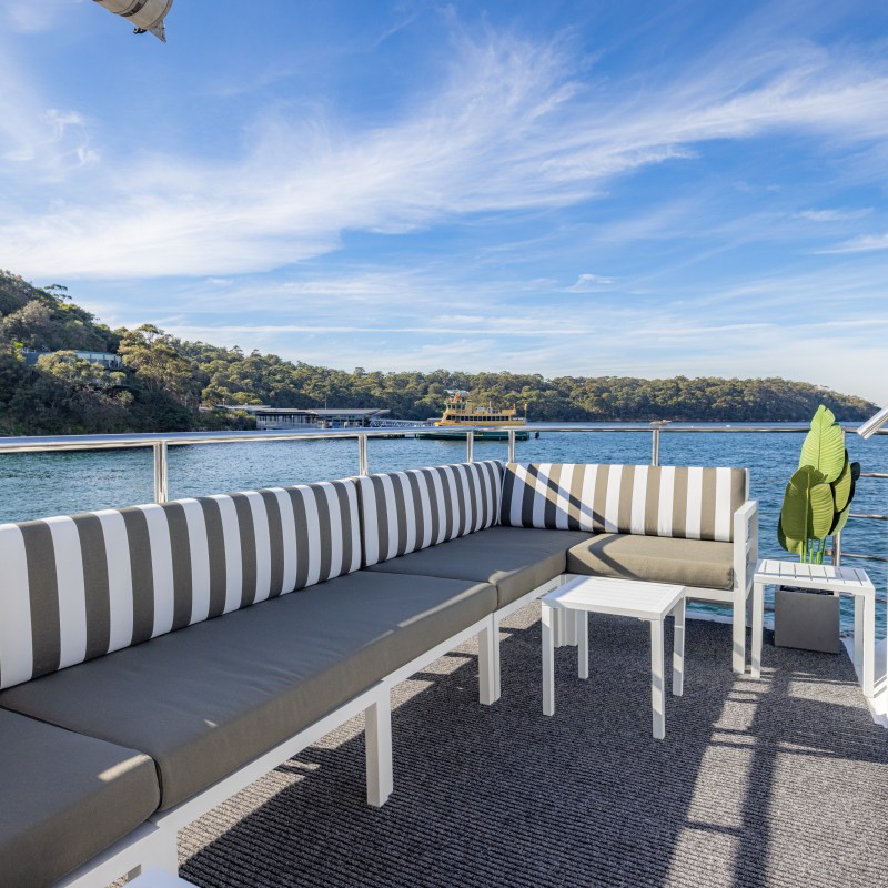 Outdoor seating on a boat with striped cushions, overlooking water and hills.