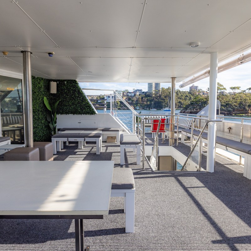 Outdoor deck with seating on a boat, view of water and trees in the background.