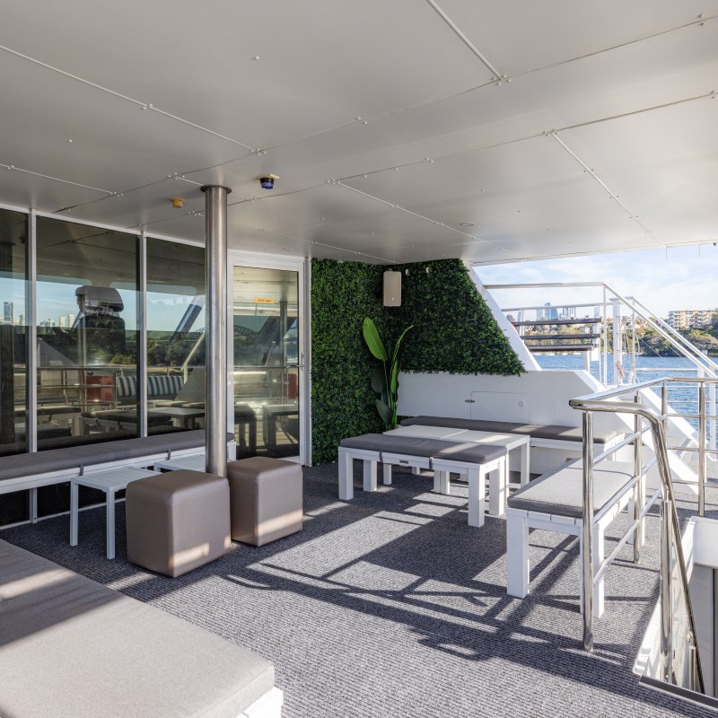 Modern boat deck with benches, a green wall, and water view in the background.
