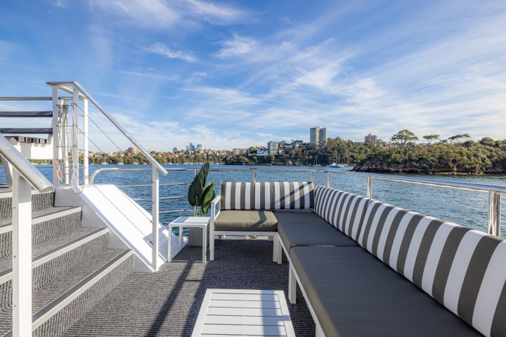 Boat deck with striped seating, stairs, and distant cityscape under a blue sky.