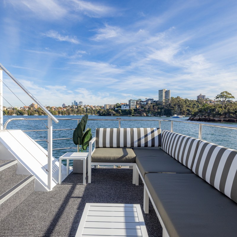 Boat deck with striped seating, stairs, and distant cityscape under a blue sky.