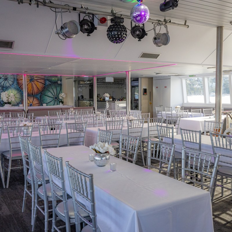 Empty banquet hall with arranged tables, white chairs, and colorful wall artwork.