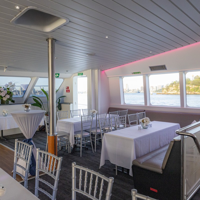 Interior of a decorated boat with tables, chairs, and windows showing a water view.