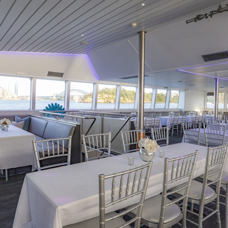 Elegant dining area on a boat with city and bridge view through windows.