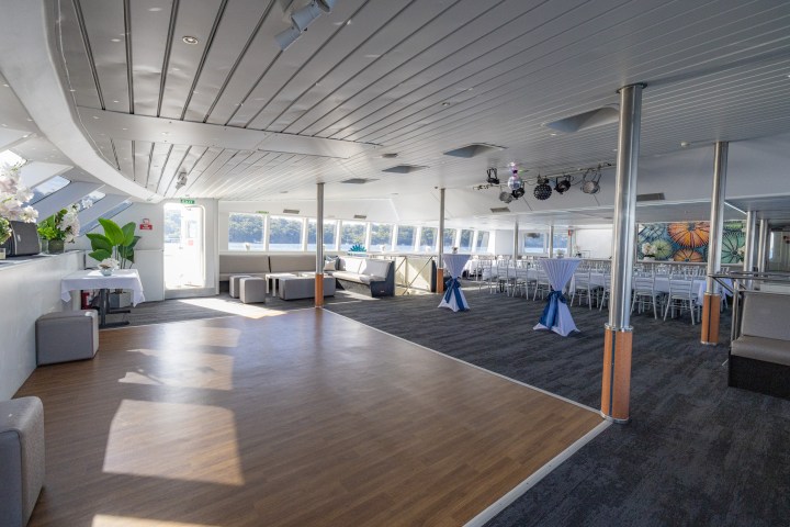 Spacious event room on a boat with tables, chairs, and windows with waterfront view.