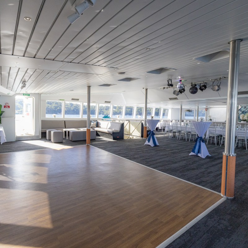 Spacious event room on a boat with tables, chairs, and windows with waterfront view.