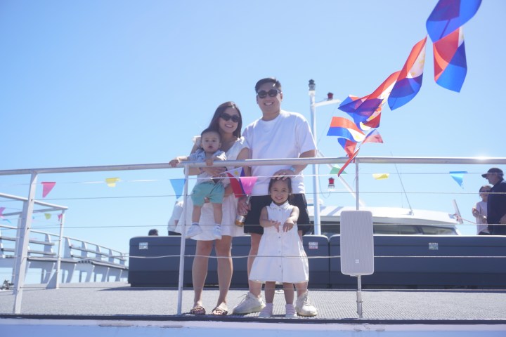 Family of four smiling on a boat deck with colorful flags and clear blue sky.