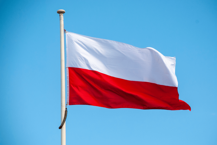 Flag of Poland waving on a pole against a clear blue sky.