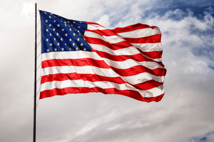 American flag waving against a cloudy blue sky background.