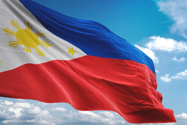 Philippine flag waving against a blue sky with clouds.