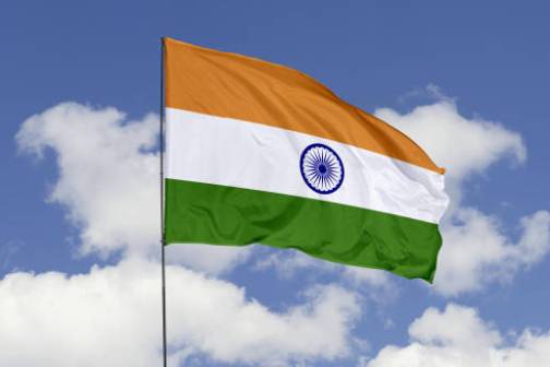 Indian flag waving against a blue sky with white clouds.