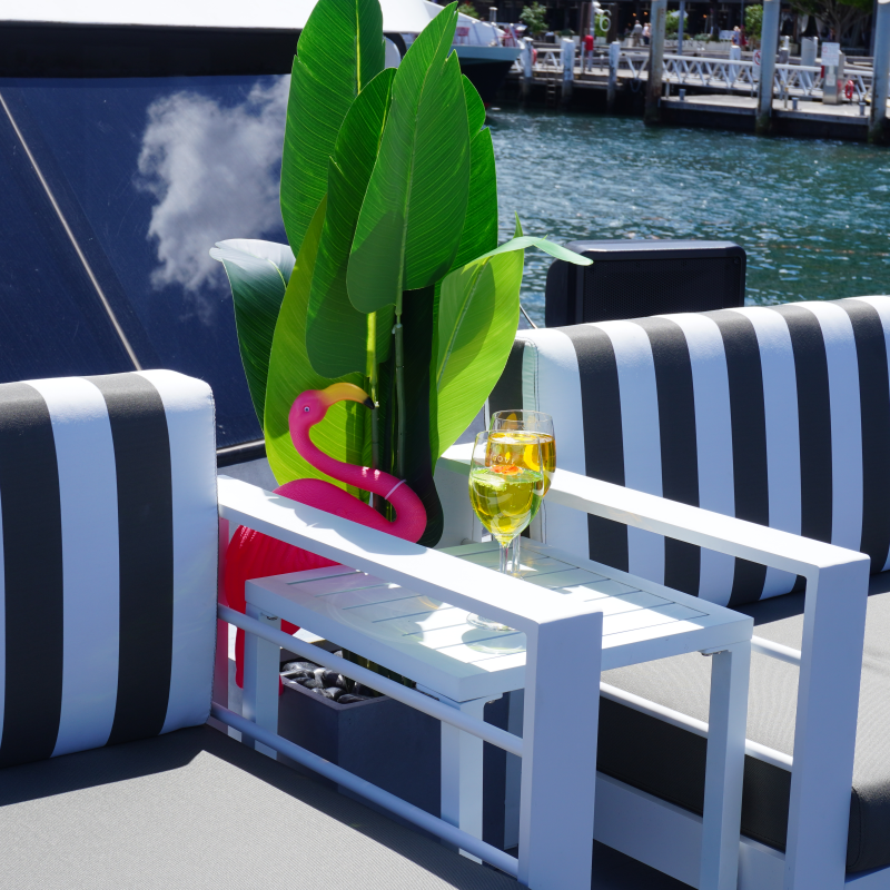 Striped outdoor seating with a glass of drink and pink flamingo decoration near water.