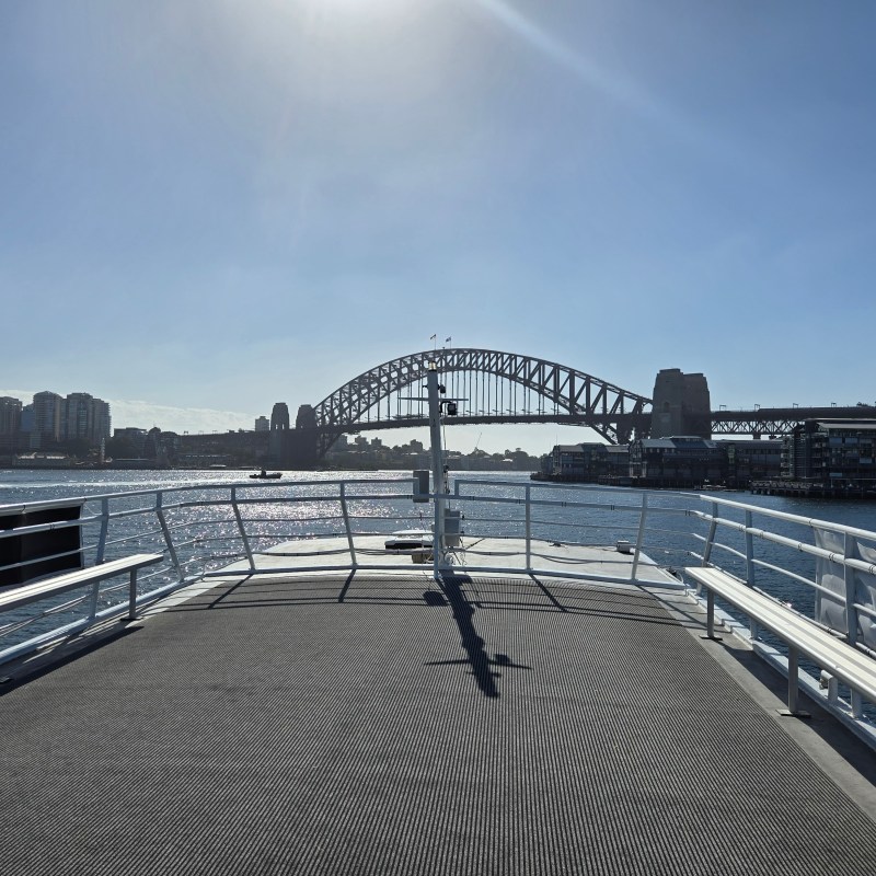 View of Sydney Harbour Bridge from a ferry deck on a sunny day.