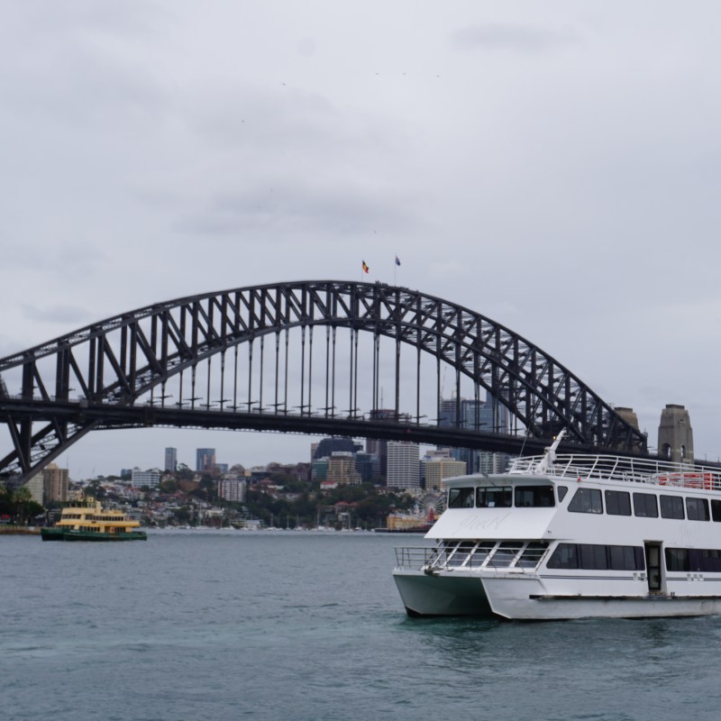 Boat on water near Sydney Harbour Bridge under cloudy sky.