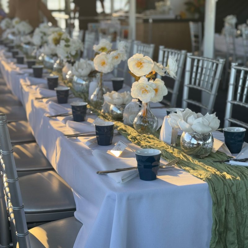 Elegantly set table with white flowers and silver chairs in a sunlit room.
